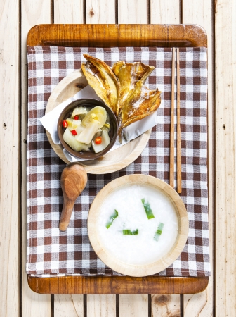 Gruel with hot and sour  pickle against fried dried fish on wooden background      の写真素材