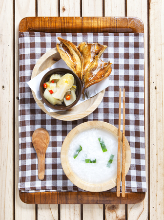 Gruel with hot and sour  pickle against fried dried fish on wooden background      の写真素材