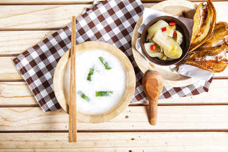 Gruel with hot and sour  pickle against fried dried fish on wooden background      の写真素材