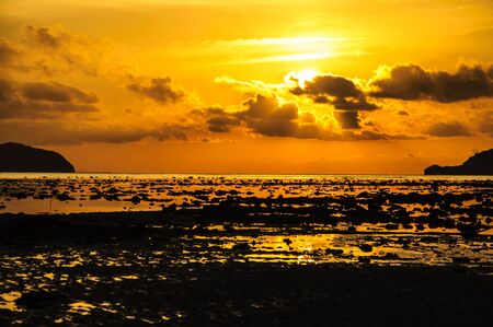 the sun rises above the sand and rock beach in winter の写真素材
