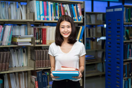 Young Student Girl Holding Book in Libraryの写真素材