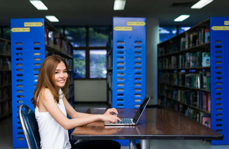 Young Girl using Laptop Computer on Table in Library Roomの写真素材