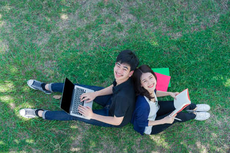 Young Students Together sitting smile on Grass open School Folders and using Laptop Computer in Education Campus University Outdoorの写真素材