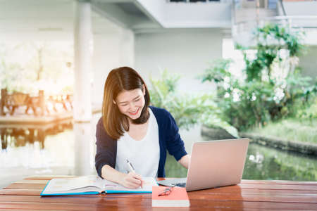 Young Girl Student Smiling Writing with School Folders Book and Laptop in Education Campus University Outdoorの写真素材