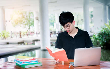 Young man student reading school book folder with laptop computerの写真素材