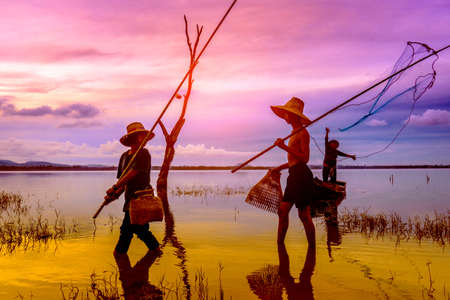 Children boy and girl walking catching fish, Fisherman fishing nets on boat at lake, river sunset thailandの写真素材
