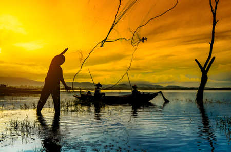 Fisherman Fishing Nets and children boy and girl on boat at lake sunset thailandの写真素材