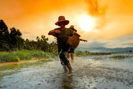 Children boy and girl run catching fish, Fisherman fishing nets on boat at lake, river sunset thailandの写真素材
