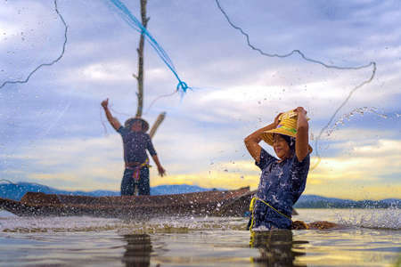 Children Fisherman Girl with catching fish splash water and fisherman throwing nets on boat on lake river thailandの写真素材