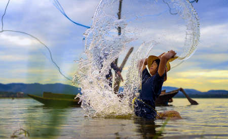 Children Fisherman Girl with catching fish splash water and fisherman throwing nets on boat on lake river thailandの写真素材