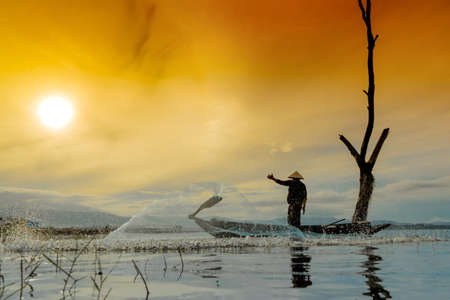 Fisherman fishing nets catching on boat at lake river sunset thailandの写真素材