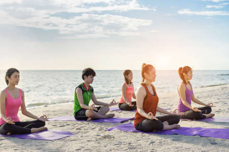 Young group yoga exercise with post on the beach in summerの写真素材