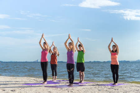 Young group yoga exercise with tree pose on the beach in summerの写真素材
