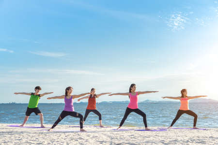 Young group yoga exercise with making warrior pose on the beach in summerの写真素材