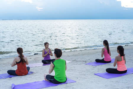 Young group yoga exercise with posting on the beach in summerの写真素材