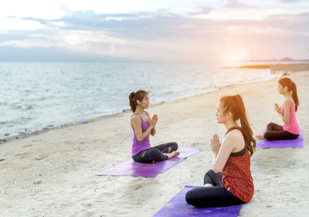 Young group yoga exercise with posting on the beach in summerの写真素材