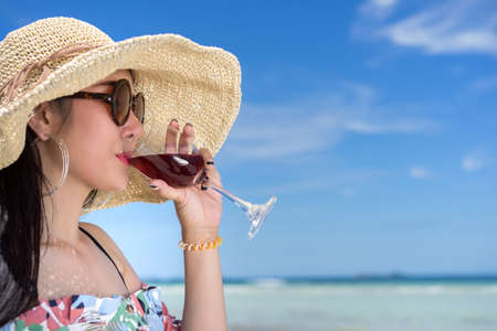 Young asian woman in hawaii dress with hat drinking wine on sea beach summer fun and happy relax in...