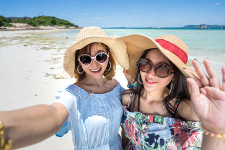 Young woman asian buddy in hawaii dress with hat selfie camera view on sea beach summer fun and happy relax in vacation timeの写真素材