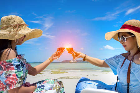 Young girl together holding wine in glass drink and cheers with sunglasses and hat on sea beach summer vacationの写真素材