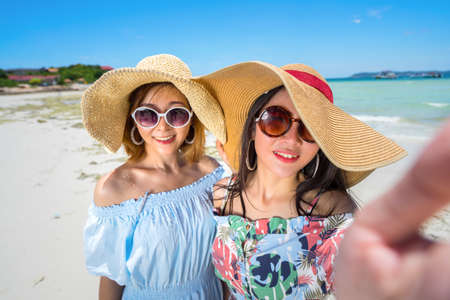 Young woman asian buddy in hawaii dress with hat selfie camera view on sea beach summer fun and happy relax in vacation timeの写真素材