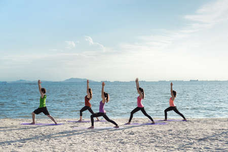 Young group yoga exercise with making warrior pose on the beach in summerの写真素材