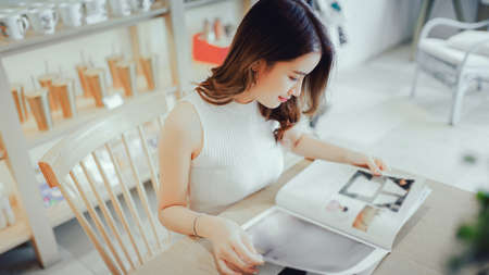 Asian young girl reading book magazine fashion smile in cafe shop with coffee brake on vacation holiday rest and relaxの写真素材