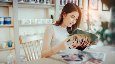 Asian young girl reading book magazine fashion smile in cafe shop with coffee brake on vacation holiday rest and relaxの写真素材