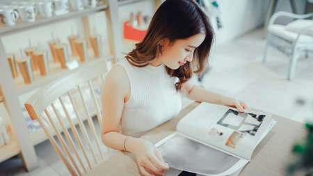 Asian young girl reading book magazine fashion smile in cafe shop with coffee brake on vacation holiday rest and relaxの写真素材