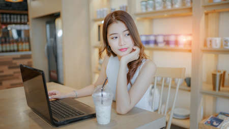 Asian young woman happiness sitting working with laptop smile in cafe shop with coffee brake on vacation holiday rest and relaxの写真素材