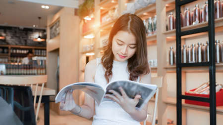 Asian young girl reading book magazine fashion smile in cafe shop with coffee brake on vacation holiday rest and relaxの写真素材