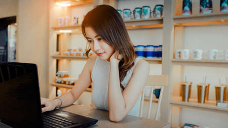 Asian young woman happiness sitting working with laptop smile in cafe shop with coffee brake on...