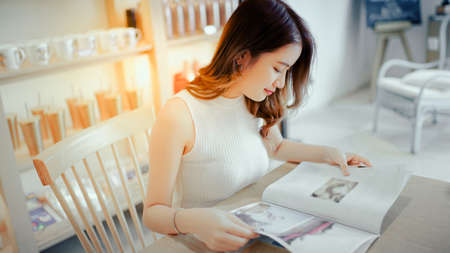 Asian young girl reading book magazine fashion smile in cafe shop with coffee brake on vacation holiday rest and relaxの写真素材
