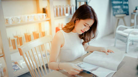 Asian young girl reading book magazine fashion smile in cafe shop with coffee brake on vacation holiday rest and relaxの写真素材