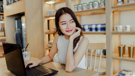 Asian young woman happiness sitting working with laptop smile in cafe shop with coffee brake on vacation holiday rest and relaxの写真素材