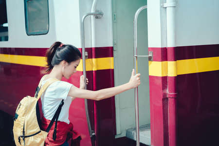 Young girl asian tourist take the train with backpack going to travel scenery town tour around at train station platform for take the rest, happy and life experience having funの写真素材