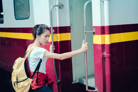 Young girl asian tourist take the train with backpack going to travel scenery town tour around at train station platform for take the rest, happy and life experience having funの写真素材