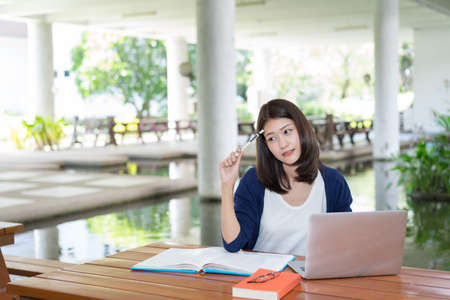 Young Girl Student Smiling Writing with School Folders Book and Laptop in Education Campus...