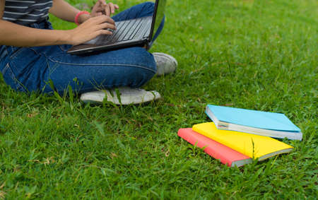 Close up Asian young girl using laptop computer with book on parkの写真素材