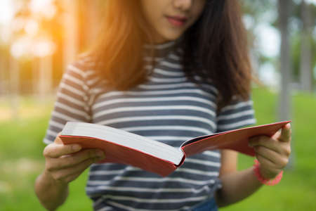 Close up Asian young girl stand reading book on park at sunset
