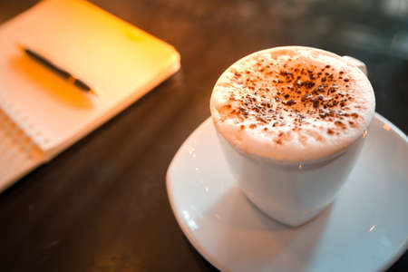 Cappuccino coffee,notebook and pen on table in the morningの写真素材