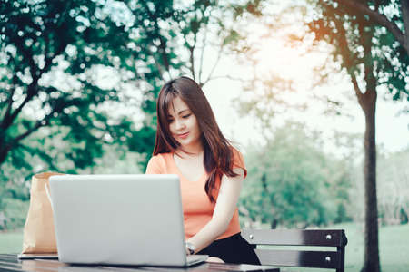 Young girl using laptop computer notebook for shopping internet online and booking with credit card for purchase in summer sale product  promotion with paper bag at park.の写真素材