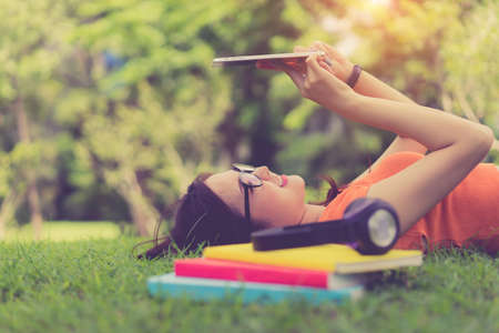 Young girl asian using tablet with headphone and school folder book relax and rest at parkの写真素材