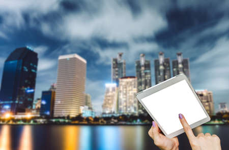 Hand hold tablet blank screen on table with Bangkok thailand cityscape with water reflection at blue...