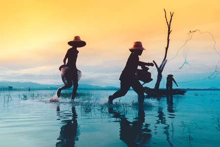 Children boy and girl catching fish, Fisherman fishing nets job lifestyle on boat at lake, river sunset thailand silhouette.の写真素材