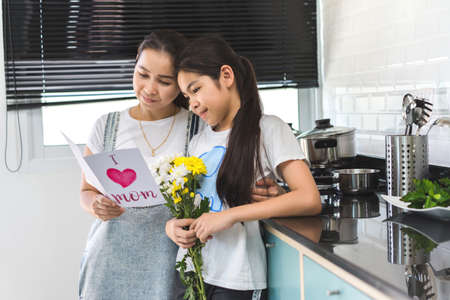 Mom reading leather postcard and children girl holding flower bouquet in home family lover or mother day happiness concept.の写真素材