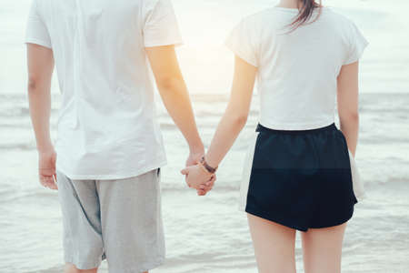 Young man holding hand with girl at sea beach in vacation summer holiday, back view close upの写真素材