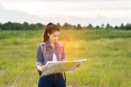 Young girl asian holding open maps for looking location to destinations with backpack travel trip in the forestの写真素材