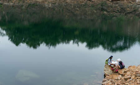 Young girl asian together with backpack sitting on big rock open maps location travel trip in the mountain and lakeの写真素材