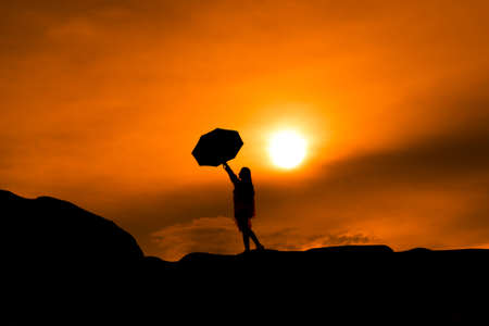 Young girl asian stand with raincoat and umbrella on mountain in the after rainy season and sunset silhouetteの写真素材