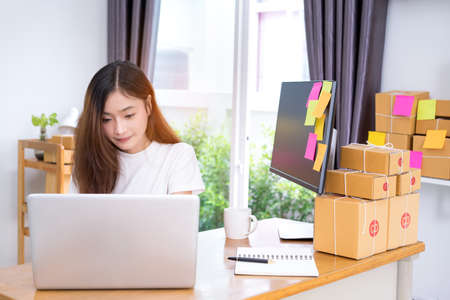 Young asian girl freelancer business private working at home office with laptop, note, coffee, packaging delivery online market on purchase orders to customer.の写真素材